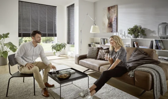 Paar unterhält sich im Wohnzimmer mit KADECO-Jalousien aus exklusivem Design-Filz