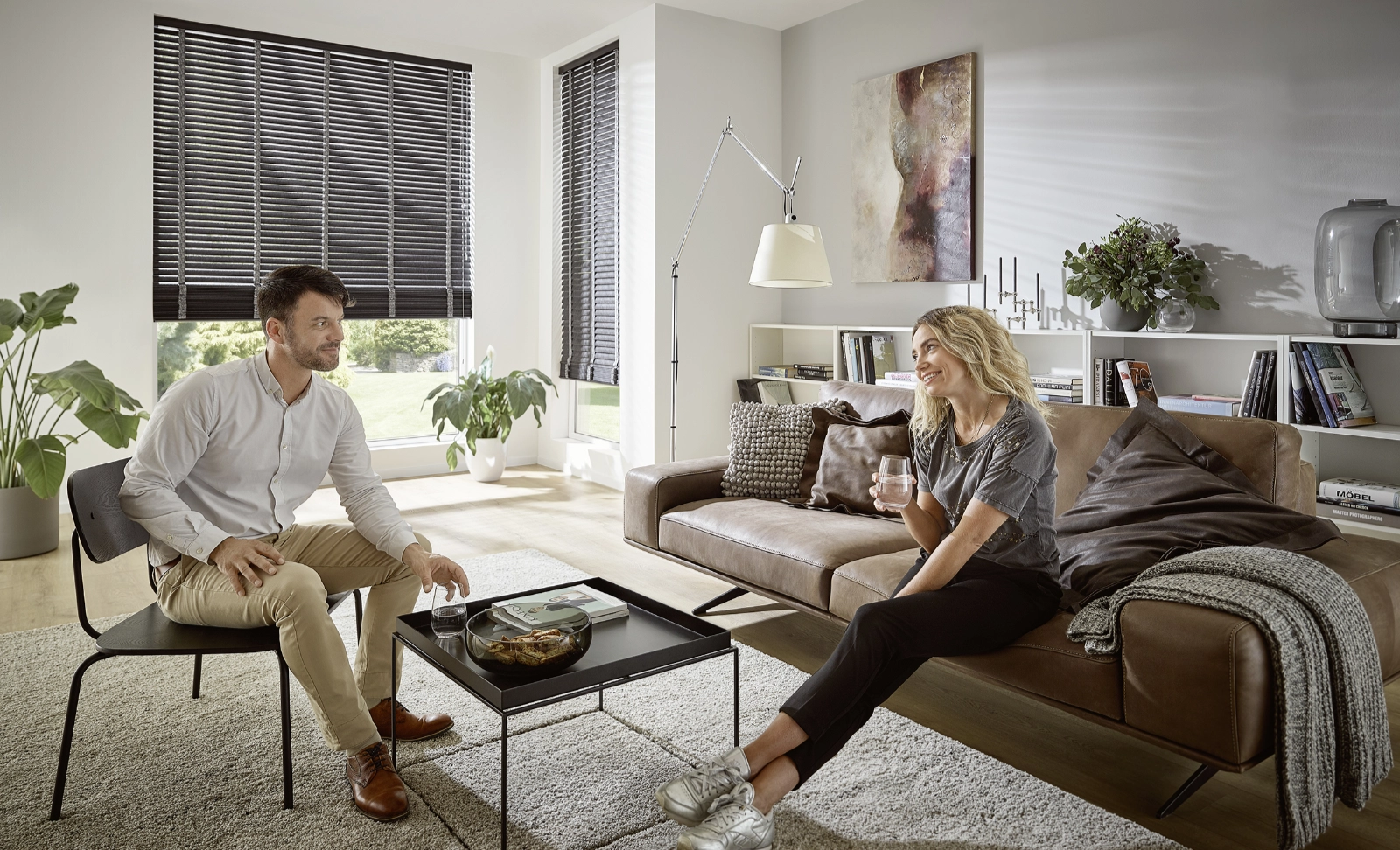 Paar unterhält sich im Wohnzimmer mit KADECO-Jalousien aus exklusivem Design-Filz